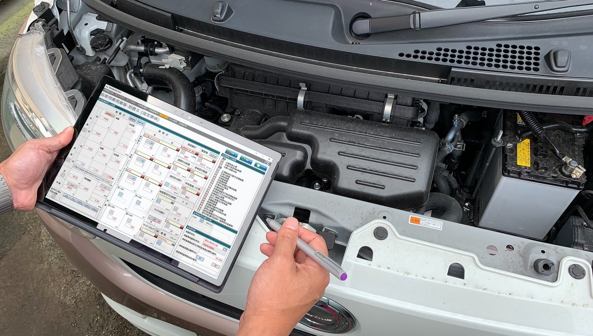 整備中の車のそばでタブレットから記録簿を入力している様子